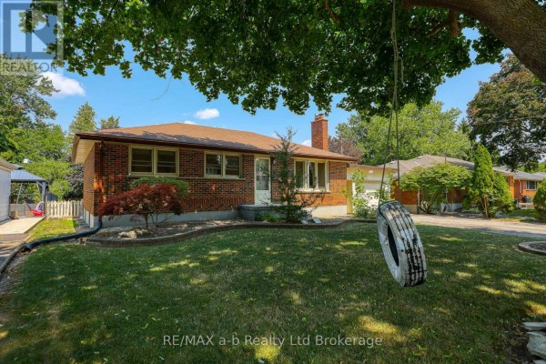 View of the side and back of a brick bungalow with a tire swing hanging from a tree. - 6752 Beattie Street, London South