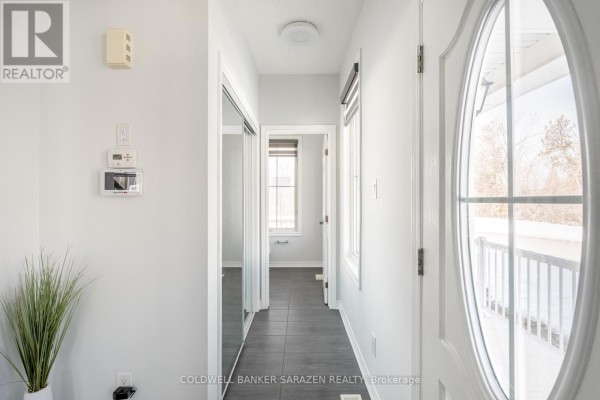 Interior view down a white hallway with grey tiled floor, a closet with mirrored doors, and a window. - 677 Broad Cove Crescent, Ottawa
