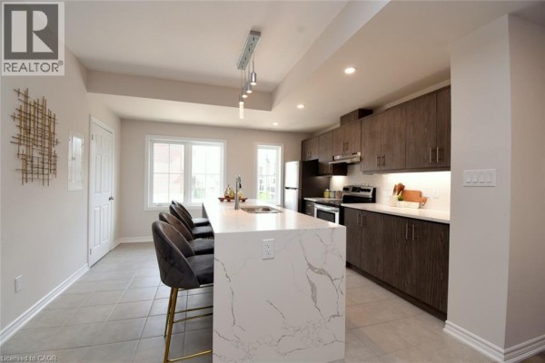 Modern kitchen with white quartz island, dark wood cabinets, and stainless steel appliances. - 677 Park Road N Unit# 2, Brantford