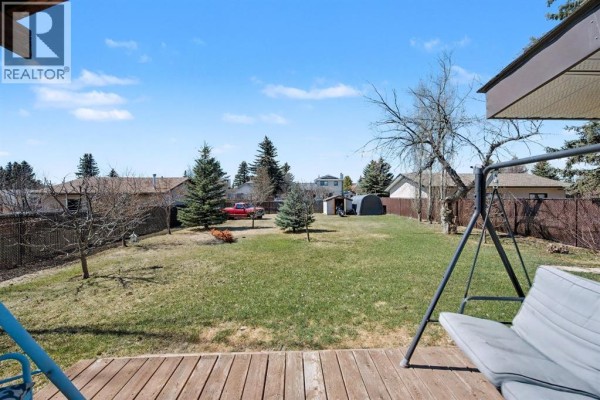 View from a wooden deck of a green backyard with trees, a swing set, and a fence. - 677 Wallace Drive, Carstairs