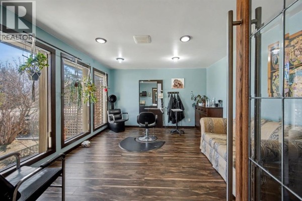 Interior room with light blue walls, dark wood floors, a salon chair, and a couch. - 677 Wallace Drive, Carstairs
