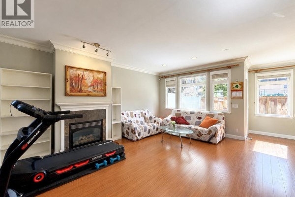Living room with fireplace, patterned sofas, treadmill, and wood floors. - 6780 Lynas Lane, Richmond