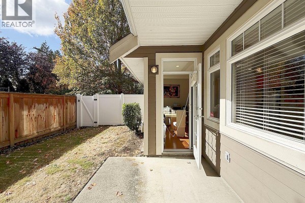 Back patio with concrete pad, grass yard, wooden fence, and doorway. - 6780 Lynas Lane, Richmond