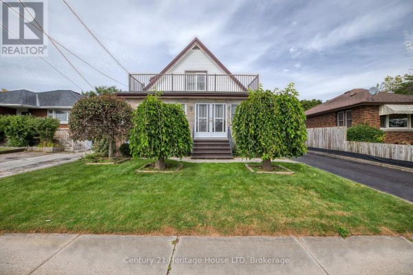 Front view of a residential house with a manicured lawn, twin trees, and a balcony on the upper level. - 6791 Dunn Street, Niagara Falls