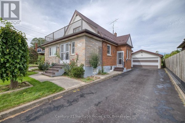 Side exterior view showcasing the brick construction, attached sunroom, driveway, and detached two-car garage. - 6791 Dunn Street, Niagara Falls