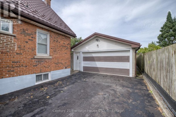 Exterior view of the detached garage with a brown and white striped door, adjacent to a wooden fence. - 6791 Dunn Street, Niagara Falls