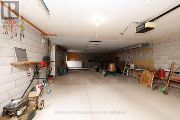 Interior view of a large, unfinished garage with concrete block walls, storage shelves, and lawn equipment. - 6791 Dunn Street, Niagara Falls