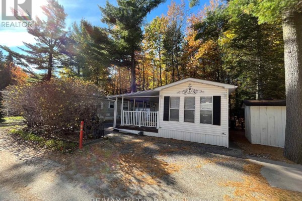Front view of white mobile home with covered porch, surrounded by trees. - 68 - 85 Theme Park Drive, Wasaga Beach