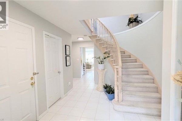 Foyer with white tile flooring, a curved staircase with wood banisters, and a view down the hall. - 68 Benjamin Drive, Hamilton