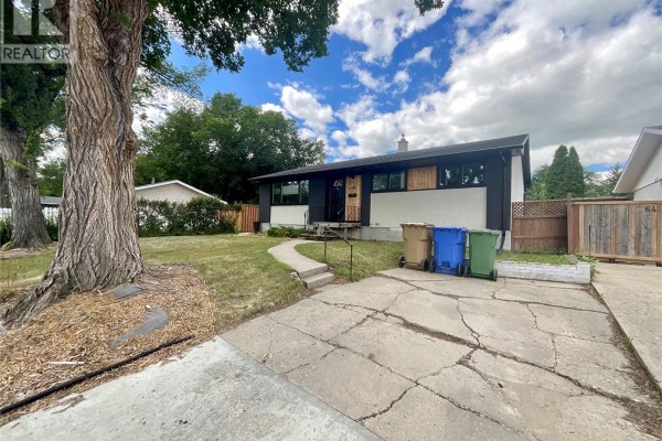 Side view of the bungalow's driveway and front lawn, with a large tree in the foreground. - 68 Cameron Crescent, Regina