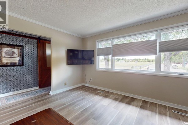 Living room with large windows, mounted television, sliding barn door, and light wood-look flooring. - 68 Cameron Crescent, Regina