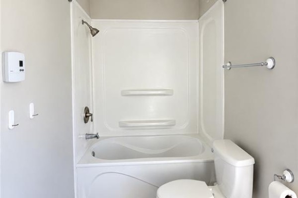 Bathroom with white bathtub, shower surround, and toilet. - 68 Cunard, Miramichi