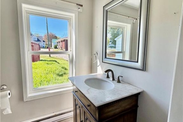 Bathroom vanity with marble countertop, dark wood cabinet, and mirror. - 68 Cunard, Miramichi