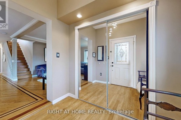 View from hallway showing a mirrored closet, interior door, and staircase with blue sofa. - 68 Eaglewood Boulevard E, Mississauga