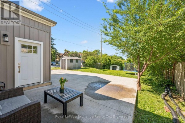 Side view of the bungalow's garage door, concrete patio with table and chairs, green tree, and backyard. - 68 Elgin Street S, Cambridge