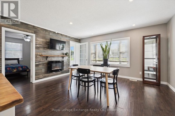 Dining area with a table and chairs, fireplace, wall-mounted TV, and large windows overlooking the backyard. - 68 Elgin Street S, Cambridge