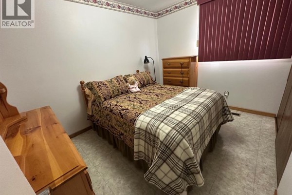 Queen bed with plaid blanket, wood dresser, and floral border - 68 Greenbriar Trail Wallaceburg