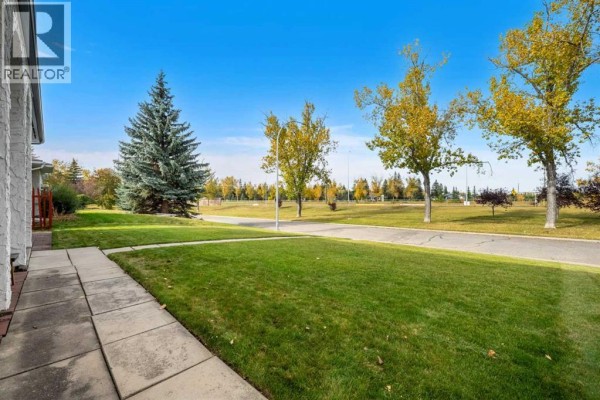 View of the green lawn and paved pathway in front of the house with trees in the background. - 68 Lake Emerald Road Se, Calgary