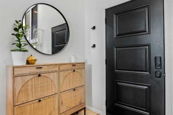 Interior entryway with a black paneled door, a round mirror, and a light wood shoe cabinet. - 68 Lake Emerald Road Se, Calgary