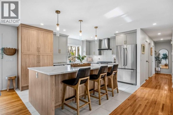 Modern kitchen with grey cabinets, a large island with a waterfall countertop, and stainless steel appliances. - 68 Lake Emerald Road Se, Calgary