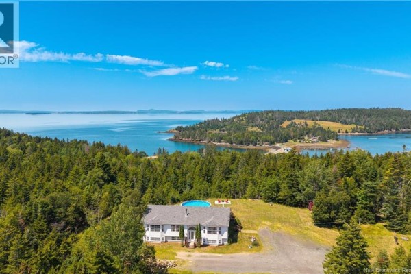 Wide aerial view of the white house, pool, forested property, and expansive water views. - 65 Lambert Road, Lamberts Cove