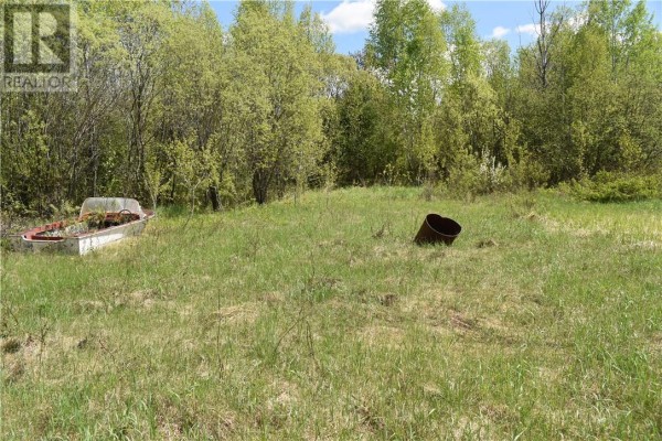 Grassy field with a rowboat and a rusted metal barrel under a cloudy sky. - 68 Lot B Plante Road, Lavigne