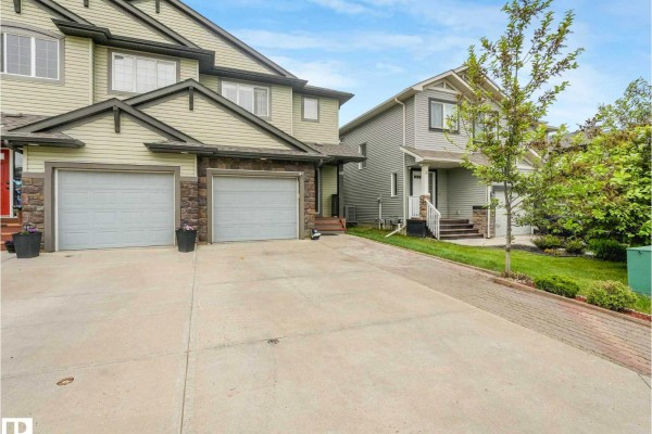 Driveway and front entrance of the duplex with two garage doors and a paved walkway. - 68 Meadowpark Ga, Spruce Grove