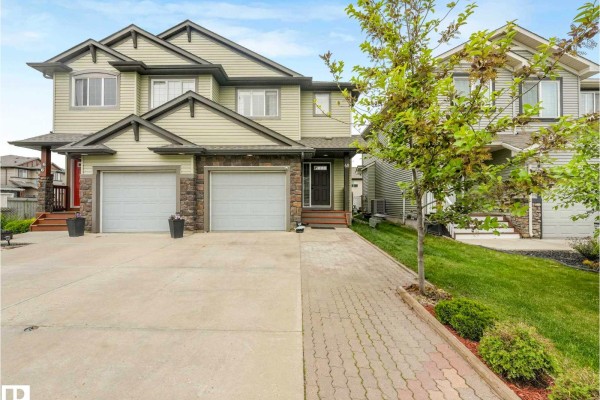 Front exterior of the duplex showcasing the light green siding, stone accents, and double garage. - 68 Meadowpark Ga, Spruce Grove