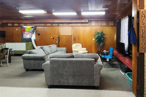 Interior room with grey sectional sofas, beige armchair, and wood paneling on walls. - 68 Tache Street, Fisher Branch