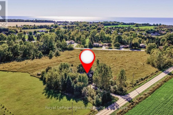 Aerial view of a property featuring a house nestled among trees, surrounded by fields and distant water. - 68 Victoria Street, Ashfield Colborne Wawanosh