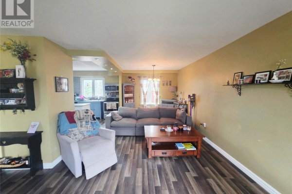 Living room with tan walls, grey sectional sofa, recliner, coffee table, and a view into the kitchen. - 68 Whiteway Drive, Wabush