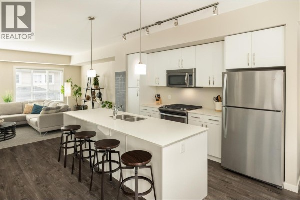 Close-up of kitchen island with quartz countertop, stainless steel oven, and modern fixtures. - 680 Old Meadows Road Unit# 81, Kelowna