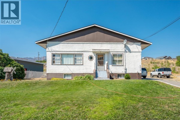 Front view of a white stucco house with a driveway and green lawn. - 6802 89th Street, Osoyoos