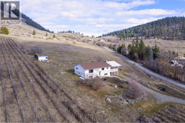 Side view of the house on a hillside with vineyards and trees surrounding it. - 6805 Reservoir Road, Grand Forks