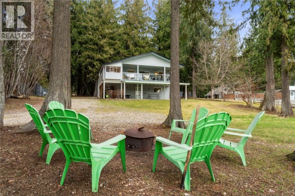 Outdoor seating area with green Adirondack chairs arranged around a metal fire pit. - 6807 Squilax - Anglemont Road, Magna Bay