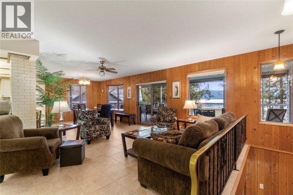 Living room with wood-paneled walls, beige tiled floors, patterned armchairs, and a brown sofa. - 6807 Squilax - Anglemont Road, Magna Bay