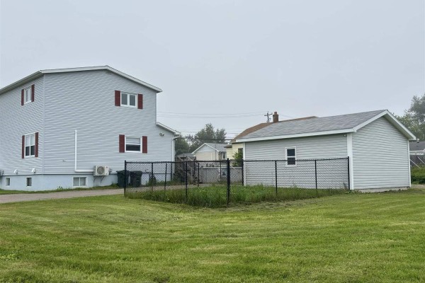 Rear view of the house showing the backyard, a chain-link fence, and a detached garage. - 683 Mahon Street, New Waterford