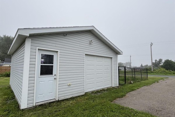 Detached garage with light grey vinyl siding, a white overhead door, and a side entrance door. - 683 Mahon Street, New Waterford
