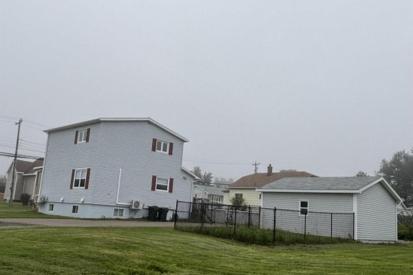 Distant view of the house and garage across a grassy yard on a foggy day. - 683 Mahon Street, New Waterford
