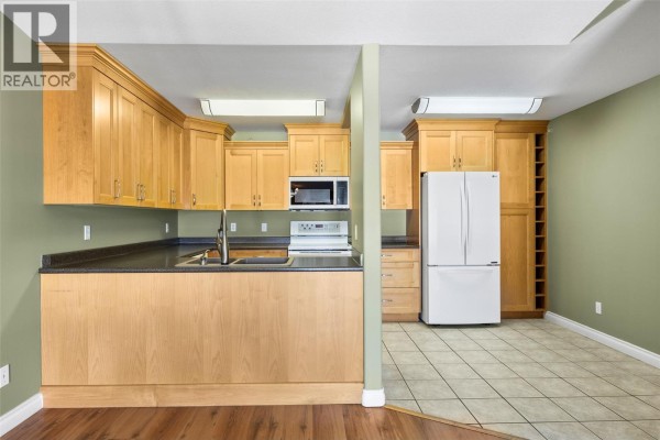 Kitchen area with light wood cabinets, dark countertops, white appliances and green walls. - 683 Victoria Street Unit# 407, Kamloops