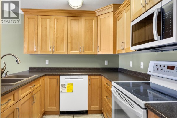 Close-up of a U-shaped kitchen with light wood cabinets, stainless steel sink, white stove and dishwasher. - 683 Victoria Street Unit# 407, Kamloops