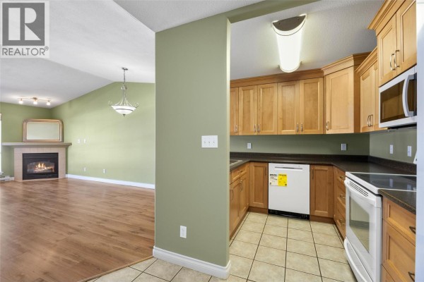 View from kitchen into living room with fireplace, wood floor and green walls. - 683 Victoria Street Unit# 407, Kamloops