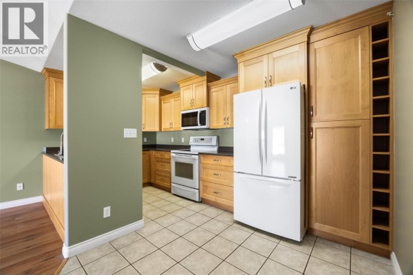 Kitchen with light wood cabinets, white refrigerator, stove, dishwasher, and a tall wine rack cabinet. - 683 Victoria Street Unit# 407, Kamloops