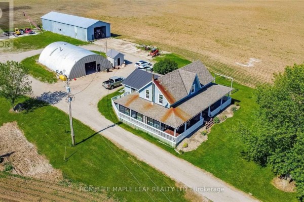 Aerial view of a blue farmhouse with a wrap-around porch and farm outbuildings. - 6830 3/4 Side Road, Clearview