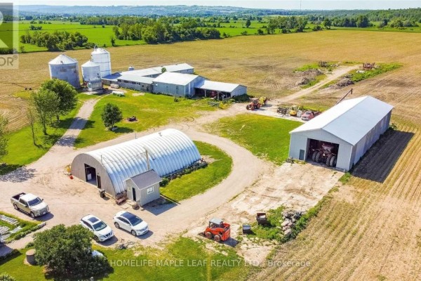 Aerial view of a farm complex with multiple barns, silos, and vehicles. - 6830 3/4 Side Road, Clearview