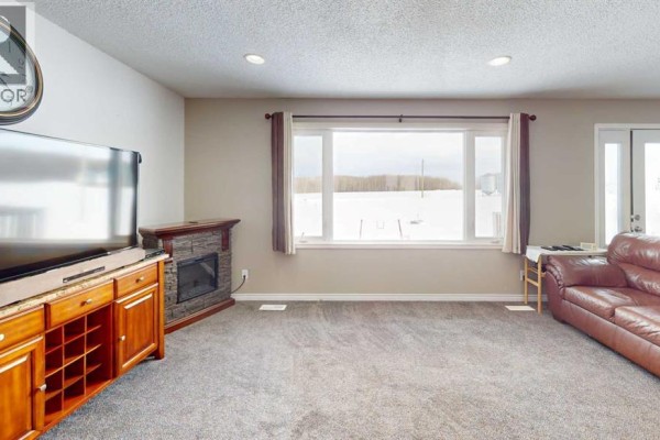 Living room with a large window, carpeted floor, and a wooden entertainment unit. - 683010 Rg Rd 175, Atmore