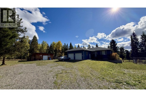 Blue house with a double garage door, adjacent to a wooden shed. - 6836 Fawn Creek Road, Lone Butte