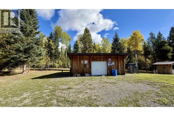 Wooden workshop with a white garage door and various signs on the exterior. - 6836 Fawn Creek Road, Lone Butte