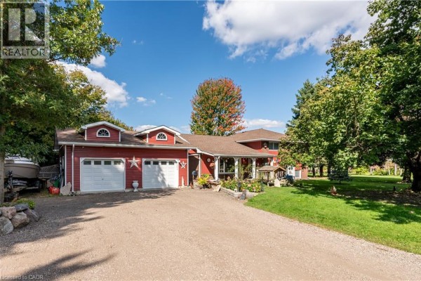 Front view of a red residential house with a three-car garage and a gravel driveway. - 685999 Kings Highway 2 Highway, Oxford County