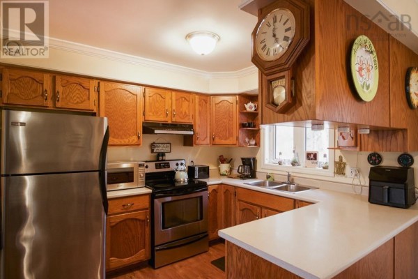 Wood-paneled kitchen with stainless steel appliances, white countertops, and a large wall clock. - 688 East Uniacke Road, Mount Uniacke